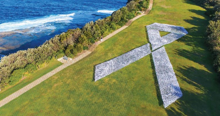 The white ribbon logo made out of white flags in a field next to the ocean